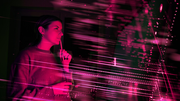 Frau, mit Stift am Mund, die nachdenklich schaut. Pinkes Licht und Lichtreflexe.