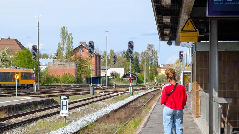 Eine Frau steht auf dem Bahnsteig und  ihre Tasche steht auf den Boden, während sie am Bahnhof Weiden in Bayern auf einen Zug wartet.