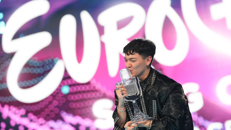 Der österreichische Sänger JJ steht auf der Bühne des ECS 2025, er ist der Gewinner. JJ hält die Gewinner-Trophäe in der Hand und küsst sie; die Trophäe st eine gläserne, mikrofonförmige Statue.