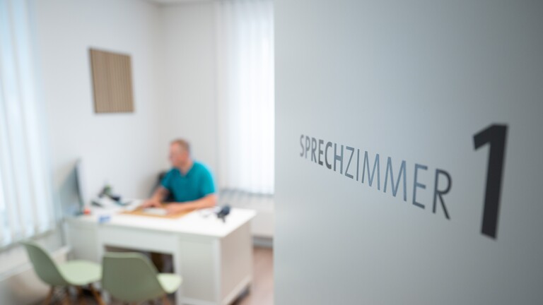 Ein Hausarzt sitzt in einem Sprechzimmer seiner Hausarztpraxis an einem Schreibtisch und arbeitet am Computer