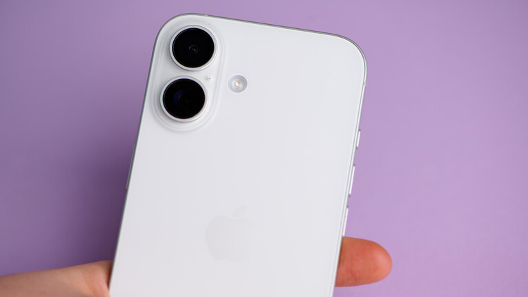 Der Nutzer hält ein schlankes weißes Apple iPhone 16 mit zwei Kameras in der Hand, das vor einem sanften lila Hintergrund steht.