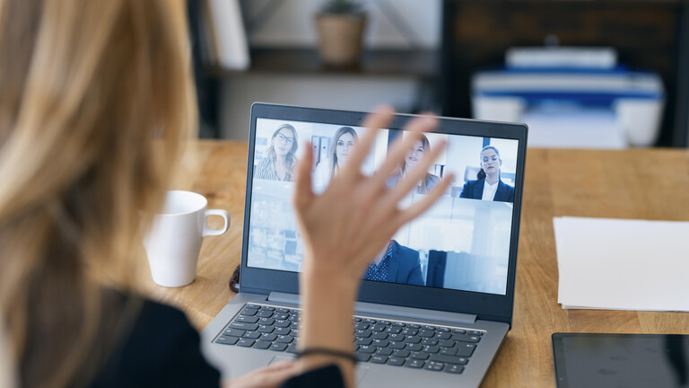 Frau hebt Hand bei Videocall in Home Office