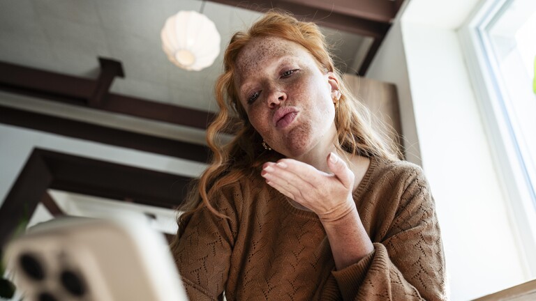 Eine Frau hält ein Smartphone in der Hand und gibt einen Luftkuss