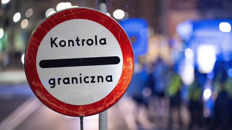 Auf einem runden Schild steht "Kontrola graniczna", polnisch für Grenzkontrolle. Im Hintergrund sind unscharf polnische Grenzschützer zu sehen.