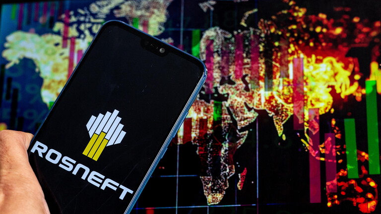 Das Rosneft-Logo auf einem Handybildschirm vor dem Hintergrund einer Weltkarte und einem Börsenchart auf einem Computerbildschirm (Symbolfoto)