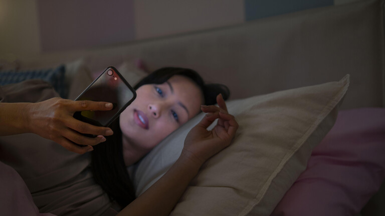 Frau mit Smartphone im Bett = Schlafstörung
