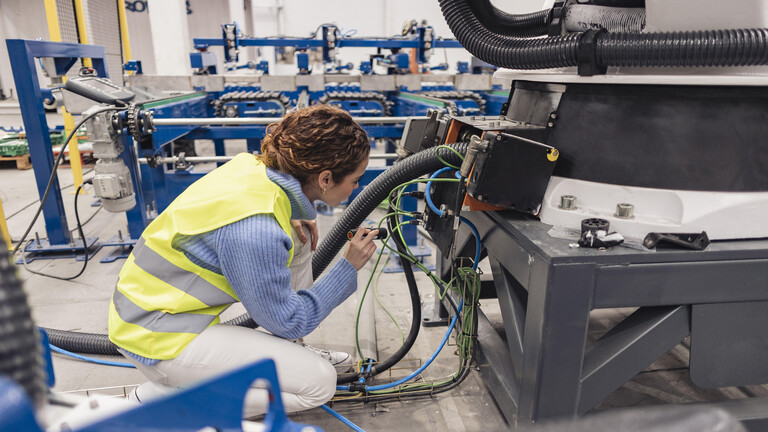 Ingenieurin untersucht in einer Fabrik ein Maschinenteil mit Taschenlampe