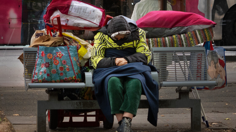 Eine Frau sitzt mit ihren Habseligkeiten in diversen Taschen auf einer Bank in Berlin