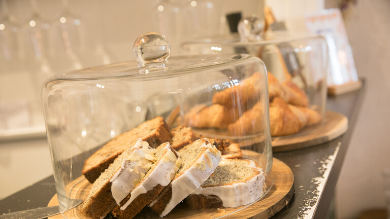 Eine Café-Theke mit Zitrone-Mohn-Kuchen, dahinter Bananenbrot und Croissants