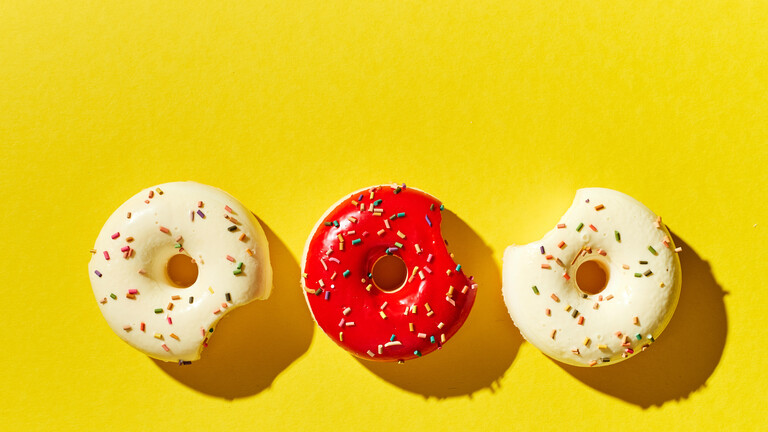 Drei Donuts, zwei in weiß und einer in rot, auf gelbem Hintergrund