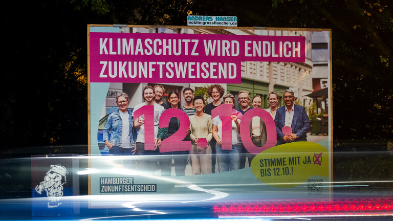 Ein Plakat für den Hamburger Zukunftsentscheid mit der Aufschrift «Klimaschutz wird endlich zukunftsweisend» steht an einer Straße (Aufnahme mit längerer Verschlusszeit).