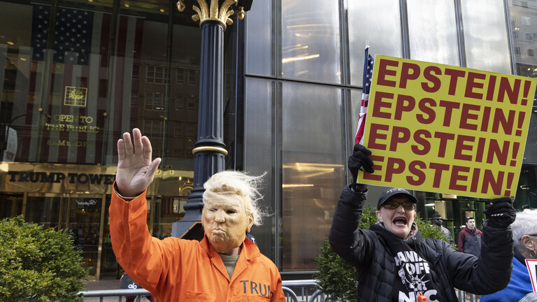 16. November 2025, New York, New York, USA: Ein Mann mit einer Trump-Maske und einem orangefarbenen Gefängnisoverall winkt Passanten auf der Fifth Avenue zu und schließt sich friedlichen Anti-Trump-Demonstranten vor dem Trump Tower an, die Schilder mit der Aufschrift „EPSTEIN! EPSTEIN! EPSTEIN! EPSTEIN!” hochhalten.