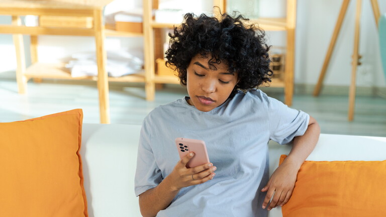 Frau sitzt auf Sofa und schaut konzentriert aufs Smartphone