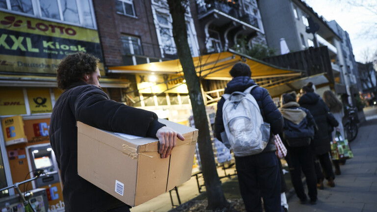 Eine Person mit einem Paket steht in einer Schlange vor einem Kiosk