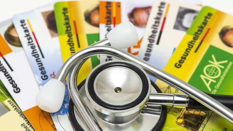Ein Stethoskop liegt auf Gesundheitskarten von verschiedenen Krankenkassen als Symbolbild für steigende Krankenkassenbeiträge und notwendige Reformen im Gesundheitssystem