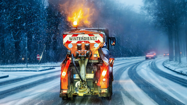 Deutschland, München, Dezember 2025, Winterdienst, Streufahrzeug im Einsatz bei Glätte und starkem Schneefall