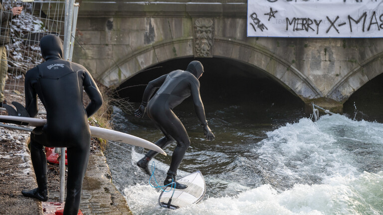 München, 29.12.2025: Nach einer nächtlichen Aktion an Weihnachten funktioniert die Eisbachwelle wieder. Ein paar Surfer genießen es. Und diie Attraktion wird wieder von Touristen besucht.