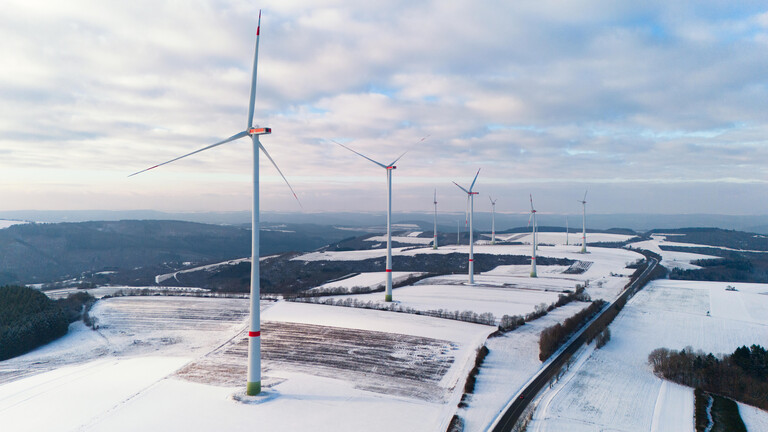 Windkraftanlagen auf einer schneebedeckten Anhöhe.