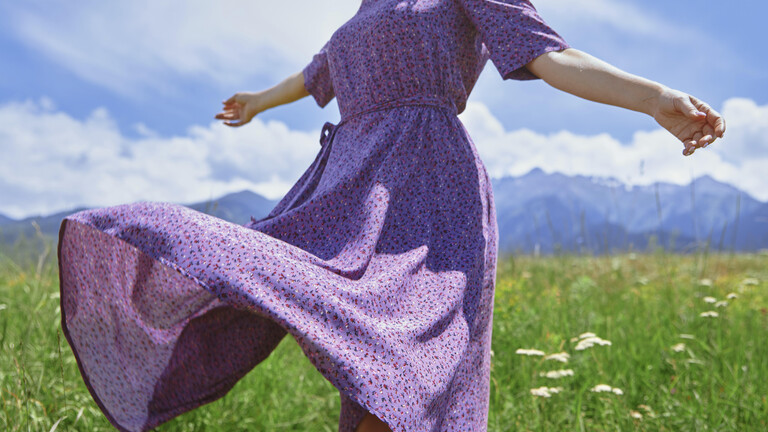 Frau in einem Blumenkleid inmitten einer grünen Wiese mit Bergen im Hintergrund, USA.