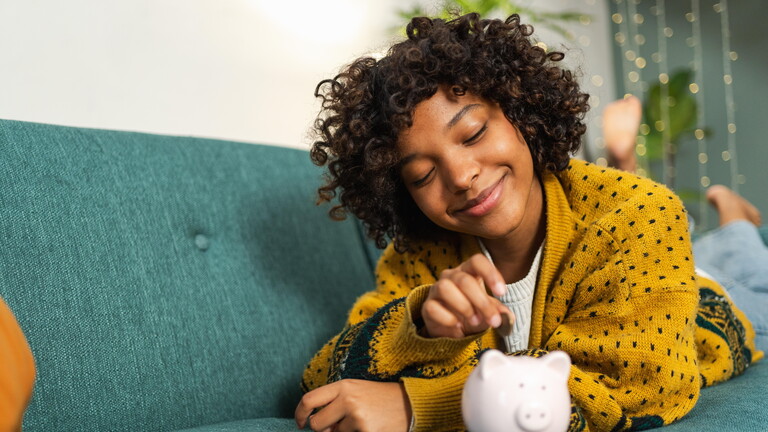 Afroamerikanisches Mädchen setzen Geldmünze in rosa Schweinchen