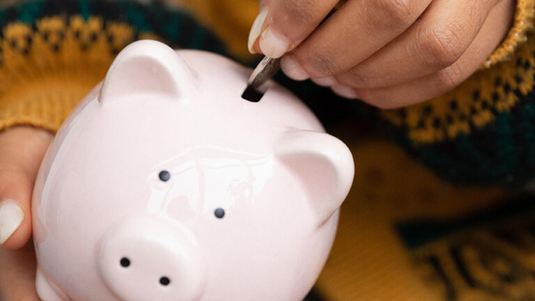 Eine Hand wirft eine Münze in ein Sparschwein