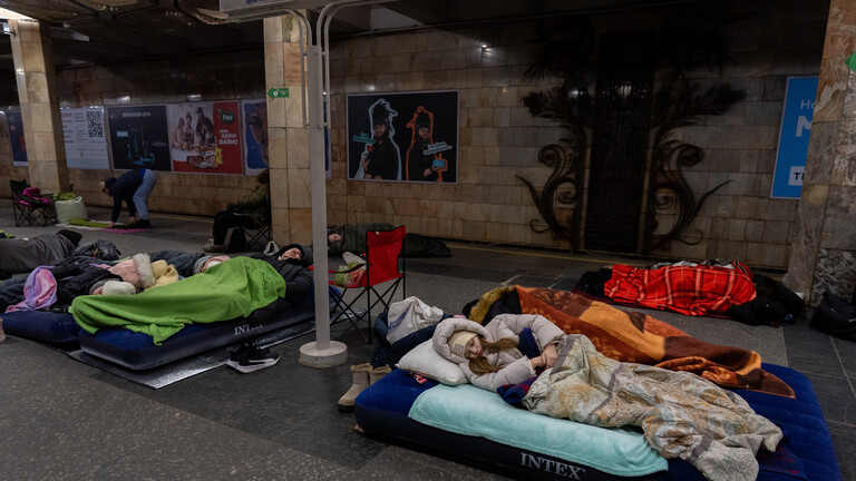 In einer U-Bahnstation in Kiew suchen Menschen nachts Schutz vor russischen Angriffen. Die Menschen tragen dicke Jacken und Mützen. Sie sind in viele Decken gehüllt und liegen auf Matratzen.