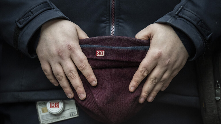 Bahnmitarbeiter hält Mütz mit DB-Logo in den Händen