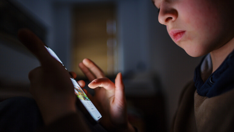Ein junge tippt im dunklen Zimmer auf den Touchscreen eines Handys