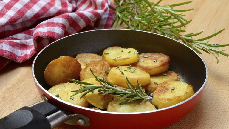 Bratkartoffeln mit Rosmarin in Pfanne auf Holzbrett