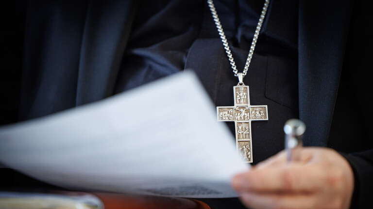 In Paderborn wird eine Studie zu sexuellem Missbrauch im Erzbistum vorgestellt. Erzbischof Bentz hält ein Papier in der Hand. Er trägt ein schwarzes Hemd und eine schwarze Jacke sowie eine Kette mit einem silbernen Kreuz. Lediglich seine Hand, das Papier und der Oberkörper sind im Bild.