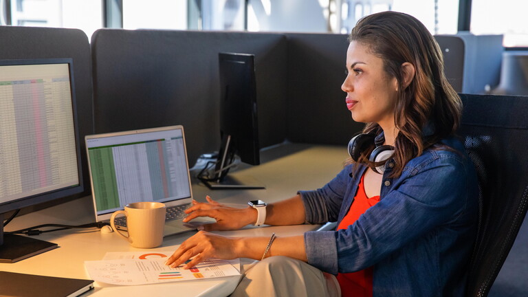 Eine Frau sitzt in einem Großraumbüro am Schreibtisch und schaut auf den Bildschirm ihres Computers.