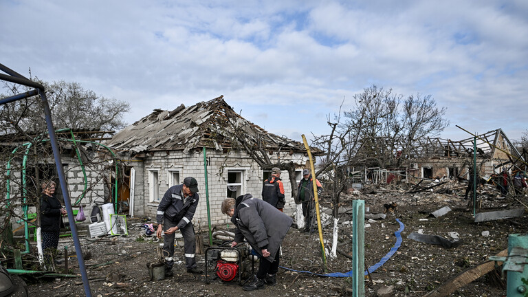 Menschen beugen sich in mitten zerstörter Häuser über einen Generator (Balabyne, Ukraine, 09.06.2026)