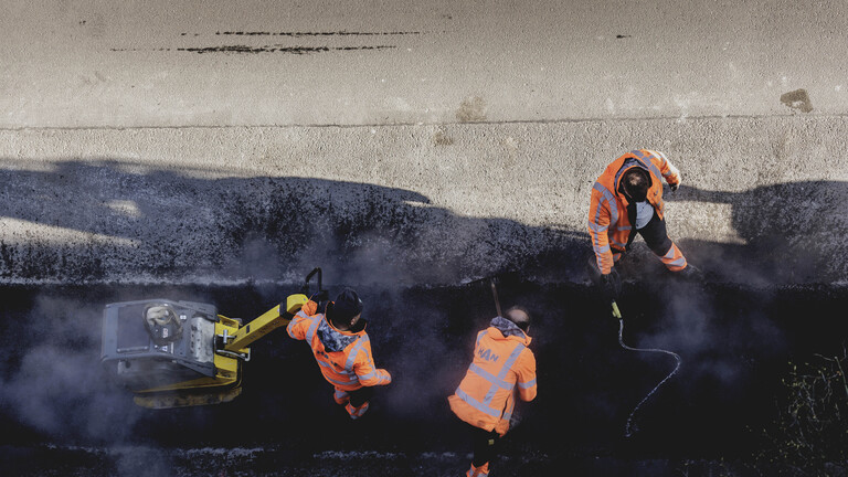 Bauarbeiter verdichten Asphalt mit einer Ruettelplatte in Berlin