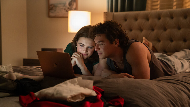 Ella Bright (l.) und Belmont Cameli liegen in der Serie "Off-Campus" auf einem Bett und schauen etwas, auf einem Laptop