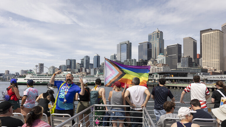 Fans auf dem Schiff „West Seattle Water Taxi“ in Downtown Seattle, große Regenbogenflagge am Schiff