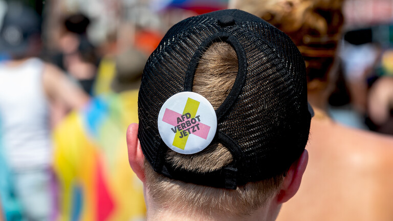 Teilnehmende Person beim Christopher Street Day (CSD) in Schleswig trägt Ansteckpin auf Cappy, auf dem „AfD Verbot jetzt“steht (27.06.2026)