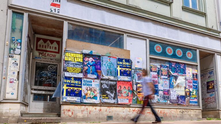 Person (verschwommen aufgenommen) geht an einem leerstehenden Geschäft in der Friedrichstraße im Zentrum von Schwerin vorbei (29.05.2026).