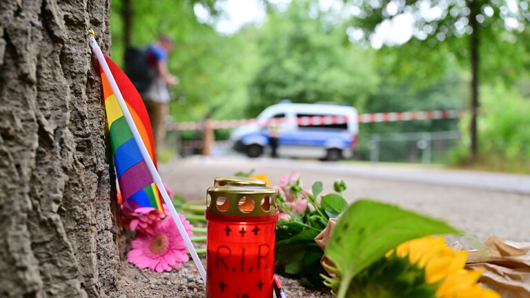 Eine Grabkerze, eine Regenbogenfahne und eine Sonnenblume liegen an einem Baum in der Nähe des Tiergartens, wo ein Auto in Teilnehmer des CSD in Berlin gefahren ist (Berlin, 26.07.2026)