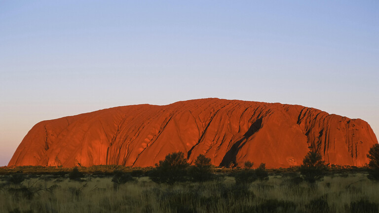 Das warme Licht der aufgehenden Sonne taucht den Uluru in ein leuchtendes Rot.
