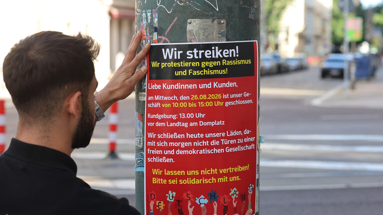 Mann bringt ein Plakat an, das zum "Migra-Streik" aufruft (Magdeburg, 25.08.2026)