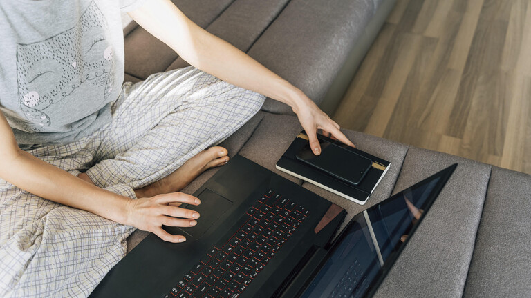In Schlafananzug gekleidete Person sitzt mit Laptop auf dem Sofa