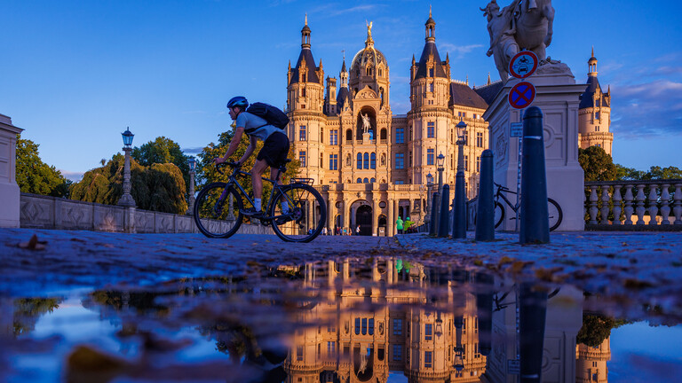 Der Landtagssitz von Mecklenburg-Vorpommern im Schweriner Schloss spiegelt sich am Abend in einer Pfütze.
