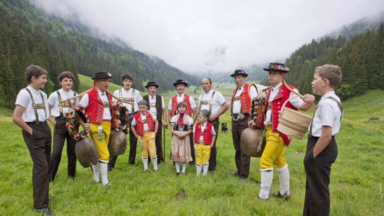 Eine Gruppe Jodler steht in einem Bergtal auf einer Wiese in Appenzell in der Schweiz. Sie tragen traditionelle Kleidung.