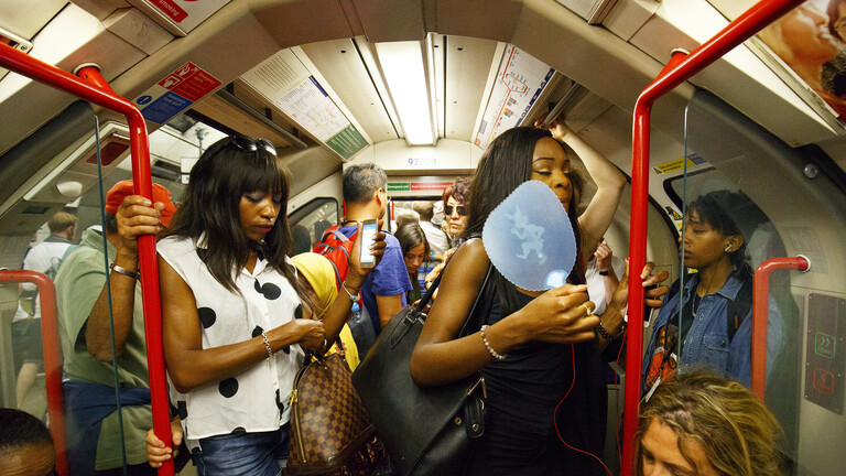 Menschen stehen und sitzen in einer vollen U-Bahn, eine Frau hat Fächer in der Hand(London, 20.07.2016)