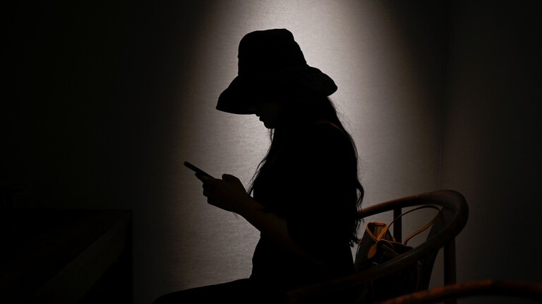 Eine Frau blickt auf ein Handy. Neben ihr befindet sich eine Tasche auf einem Stuhl