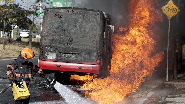 Einsatzkraft der Feuerwehr löscht auf einer Hauptstraße in Zapopan einen brennenden Bus (Mexiko, 22.02.2026)