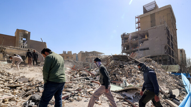 Drei Personen gehen an zerbombten Gebäude in Teheran entlang (3.03.2026, Iran)