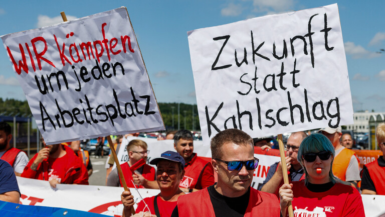 Mitarbeiter von Volkswagen (VW) halten bei einer von der IG Metall organisierten Kundgebung Schilder mit den Aufschriften „Wir kämpfen um jeden Arbeitsplatz“ (links) und „Zukunft statt Kahlschlag“ in die Höhe (9.07.2026, Zwickau)