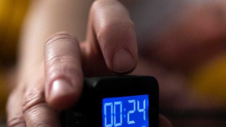 Mann liegt im Bett und schaltet seinen Wecker ein.