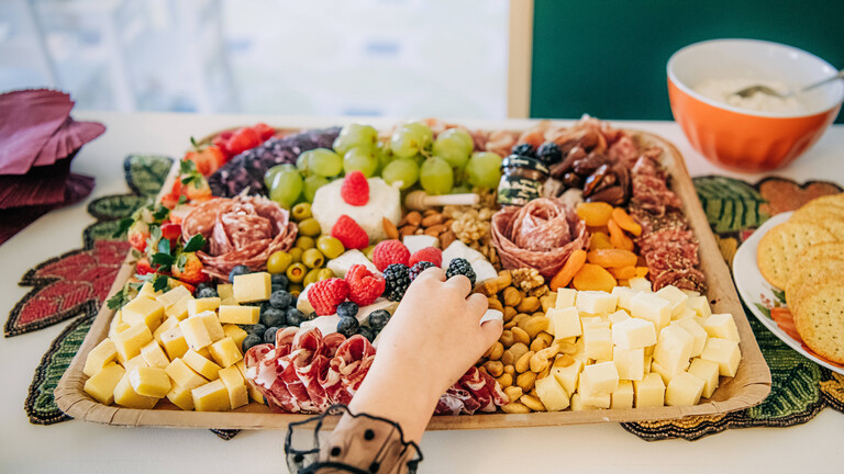 Eine Hand greift nach einem Objekt auf einem Blech übervoll mit Lebensmitteln